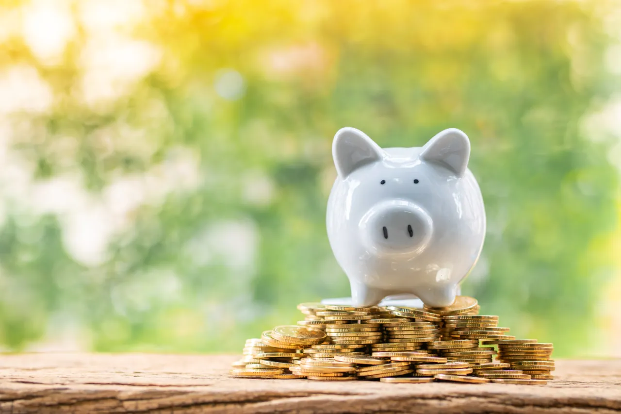 Weißes Sparschwein auf einem Stapel Goldmünzen vor grünem Hintergrund